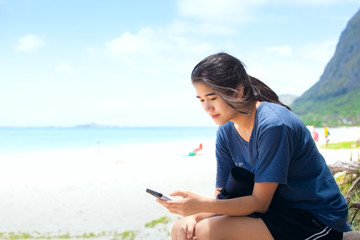Biracial teen girl sitting on Hawaiian beach looking at smartphone