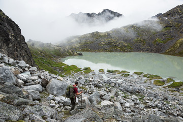 Hiker descending toward green glacial lake in Hatcher Pass area of Alaska