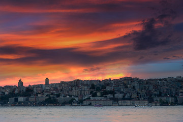 Landscape of Istanbul at sunset. View of dramatic cloudy sky and lights business district from sea. Turkey.
