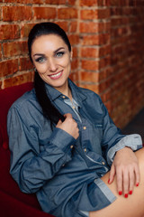 Pretty smiling brunette woman in shirt near brick wall.