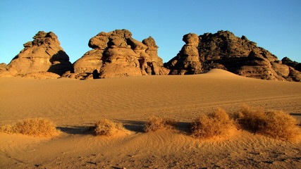 dunkle Sandsteinberge erheben sich aus der Sandwüste im Abendlicht