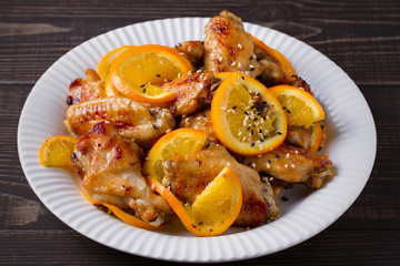 Sweet and sour chicken wings with oranges, served with sesame on white plate