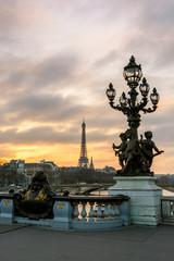 Fototapeta na wymiar View of the Eiffel tower from the Pont Alexandre III at sunset with one of its Art Nouveau street lamp, ornamented with cherubs, in the foreground.