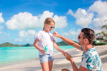 Young father applying sun cream to daughter nose on the beach. Sun protection