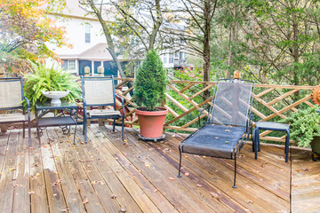 Closeup of wooden deck of house with many green plants, trees, tables, chairs, on rainy overcast day, decorations