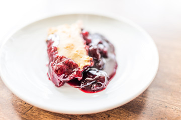 Closeup of hot fresh red cherry cobbler slice piece on white plate on table golden crust, gooey thick filling