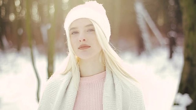 Beautiful blond girl in a white cap walks in the winter forest. The girl goes to the camera