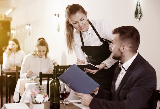Welcoming female waiter is taking order from businessman in rest