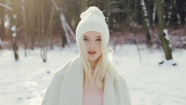 Beautiful blond girl in a white cap walks in the winter forest. The girl goes to the camera