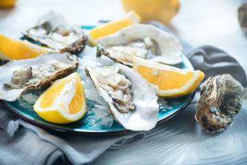 Fresh oysters close-up on blue plate, served table with oysters, lemon in restaurant. Gourmet food