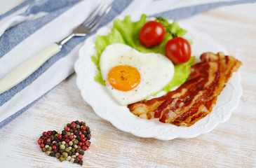 Fototapeta na wymiar Tasty Fried Egg in the Shape of a Heart Served on a White Plate Bacon Pepper Tomato Salad Leaves Wooden Background Valentine Day Morning