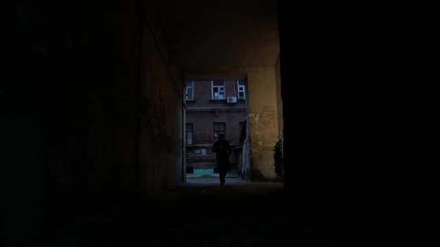 4k Alone man in coat goes through the dark noir arch in cold city