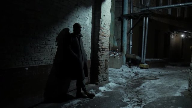 4k Middle age man standing at the wall at cold night getaway and waiting for someone at winter city