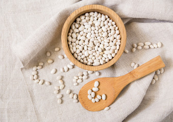 white kidney beans.wooden plate and spoon.coarse woven tablecloth.top view