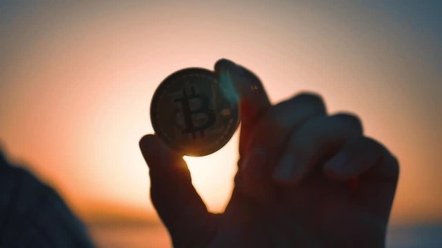 Golden bitcoin coin in hand on a blurred sunset background.