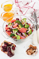 Broccoli salad / Broccoli, pomegranate, grapefruit salad with walnut, red onion, honey and olive oil in glass bowl on white wooden background