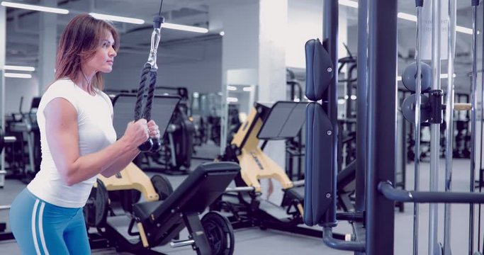 Adult woman doing Exercises for Tricep in fitness gym. Beautiful Woman doing triceps workout. Fitness girl doing triceps cable pushdown exercise in gym