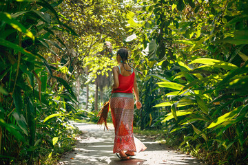 Cheerful young boho style woman walking by the road with tropical background