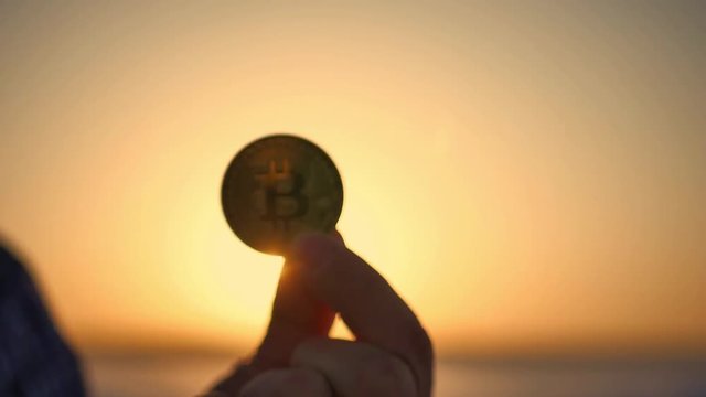 Golden bitcoin coin in hand on a blurred sunset background.