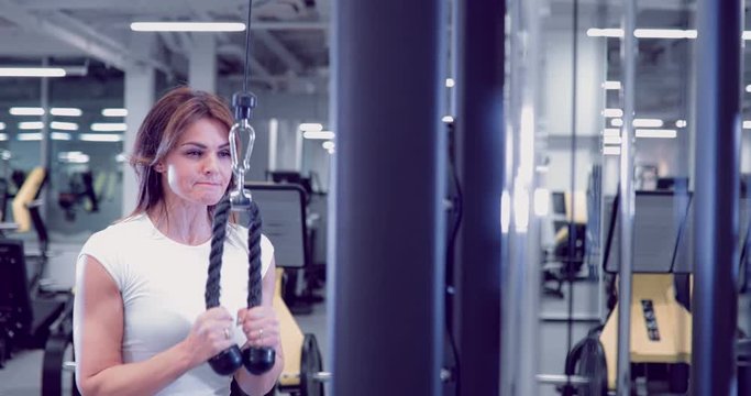 Adult woman doing Exercises for Tricep in fitness gym. Beautiful Woman doing triceps workout. Fitness girl doing triceps cable pushdown exercise in gym
