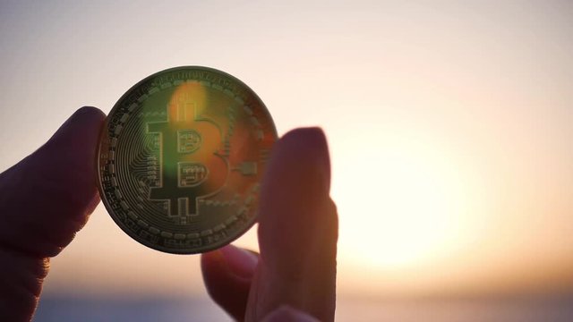 Golden bitcoin coin in hand on a blurred sunset background.
