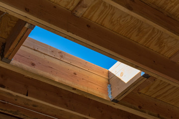 Residential roof construction seen from interior with skylight detail and blue sky, horizontal aspect