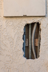 View of electrical conduit seen through a hole in the exterior stucco of a home leading to the panel box, copy space, vertical aspect
