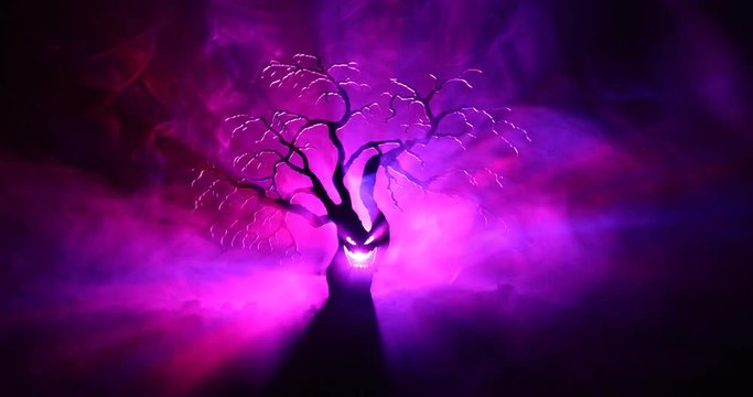 Silhouette of scary Halloween tree with horror face on dark foggy toned background with moon on back side. Scary horror tree with zombie and monster demon faces.