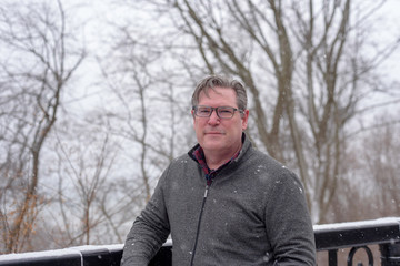 Handsome confident middle aged man with glasses leaning against a railing at the park in winter