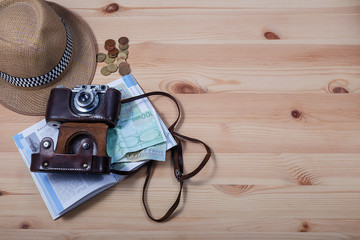 Accessories for travelers. Camera, hat, seashell with money and book guides on wooden background. Top view with copy space