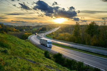 Trucks driving on the highway turning towards the horizon in an autumn landscape at sunset with dramatic clouds. Electronic toll gate in the middle.