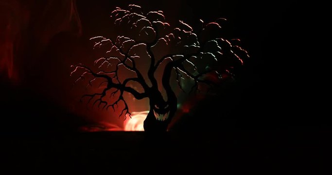 Silhouette of scary Halloween tree with horror face on dark foggy toned background with moon on back side. Scary horror tree with zombie and monster demon faces.
