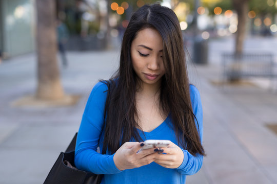 Young Asian woman walking texting cell phone