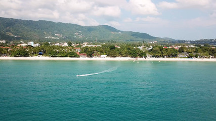Fototapeta na wymiar Aerial view of white sand beach and jet ski on the blue lagoon aqua sea. Aerial bird's eye view of jet ski cruising in high speed in turquoise clear water sea