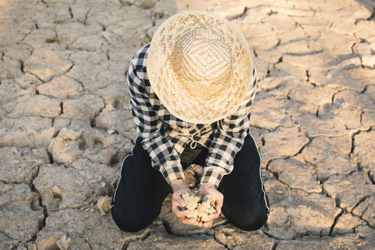 Asian man holding soil on cracked dry ground, concept drought and crisis environment