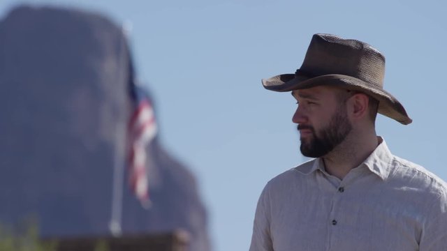 Cowboy man putting on hat in front of american flag