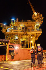 Two worker in offshore oil and gas operation discussion about platform before transfer to working on platform in night ship during stand in supply boat - obrazy, fototapety, plakaty