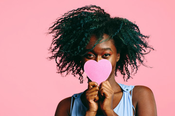 Portrait of young woman holding pink heart in front of face