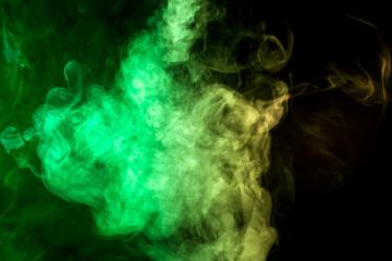 Obraz na płótnie Canvas Thick colorful smoke of green and yellow on a black isolated background. Background from the smoke of vape
