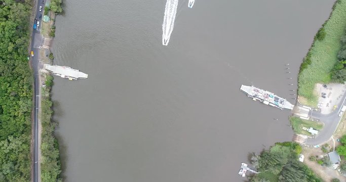 Car carrying ferries over Hawkesbury river at Wisemans ferry town crossing river with car cargo in aerial top down.
