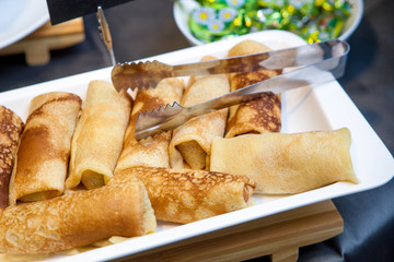 Close-up of breakfast on a buffet: stuffed pancakes with meat and rice on a white plate
