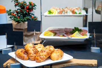 Close-up breakfast on a buffet: fresh pastry patties with a filling on a white plate, sliced red fish, and rolls