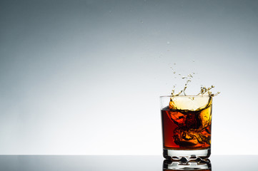 A splash of orange drink in a transparent glass on the right frame on a blue background.