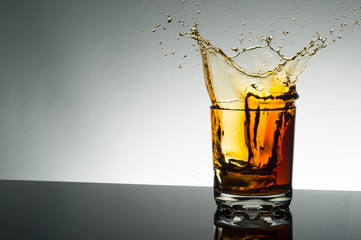 A splash of a yellow drink in a glass with ice.