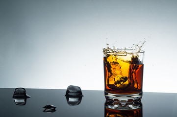 A splash of whiskey with ice in a glass on a flat surface on a light background with an empty space for text.