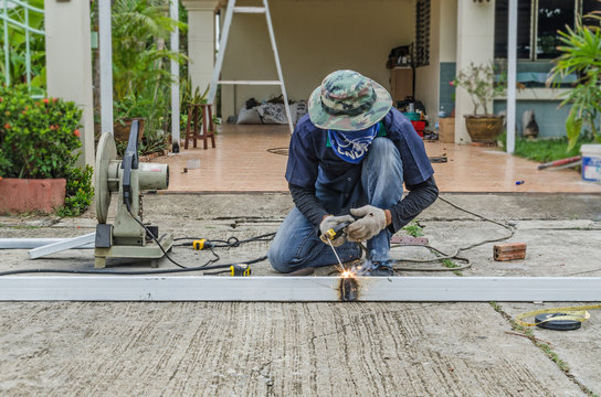 asian worker with machine cutting metal and welded steel to create a roof, local labor construction concept