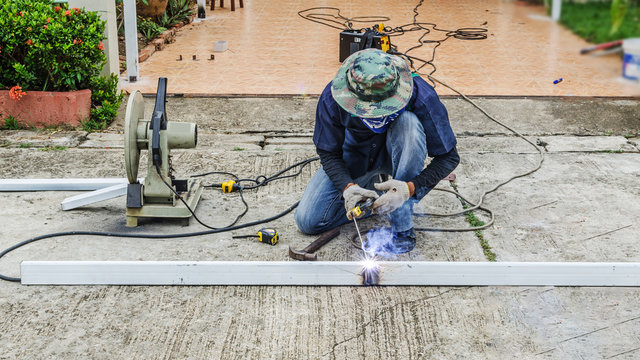 asian worker with machine cutting metal and welded steel to create a roof, local labor construction concept