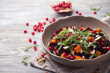 Salad with black rice, baked pumpkin, pomegranate seeds, arugula and nuts on a gray background. Delicious vegan food