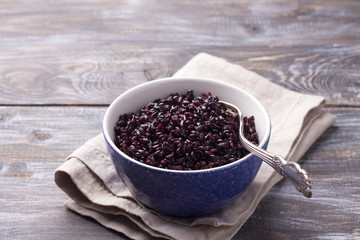 Black rice in a blue bowl on a wooden table, selective focus, rustic style. Simple healthy food