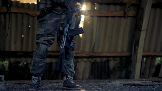 A combatant in army fatigues takes a rifle from the shoulder. 